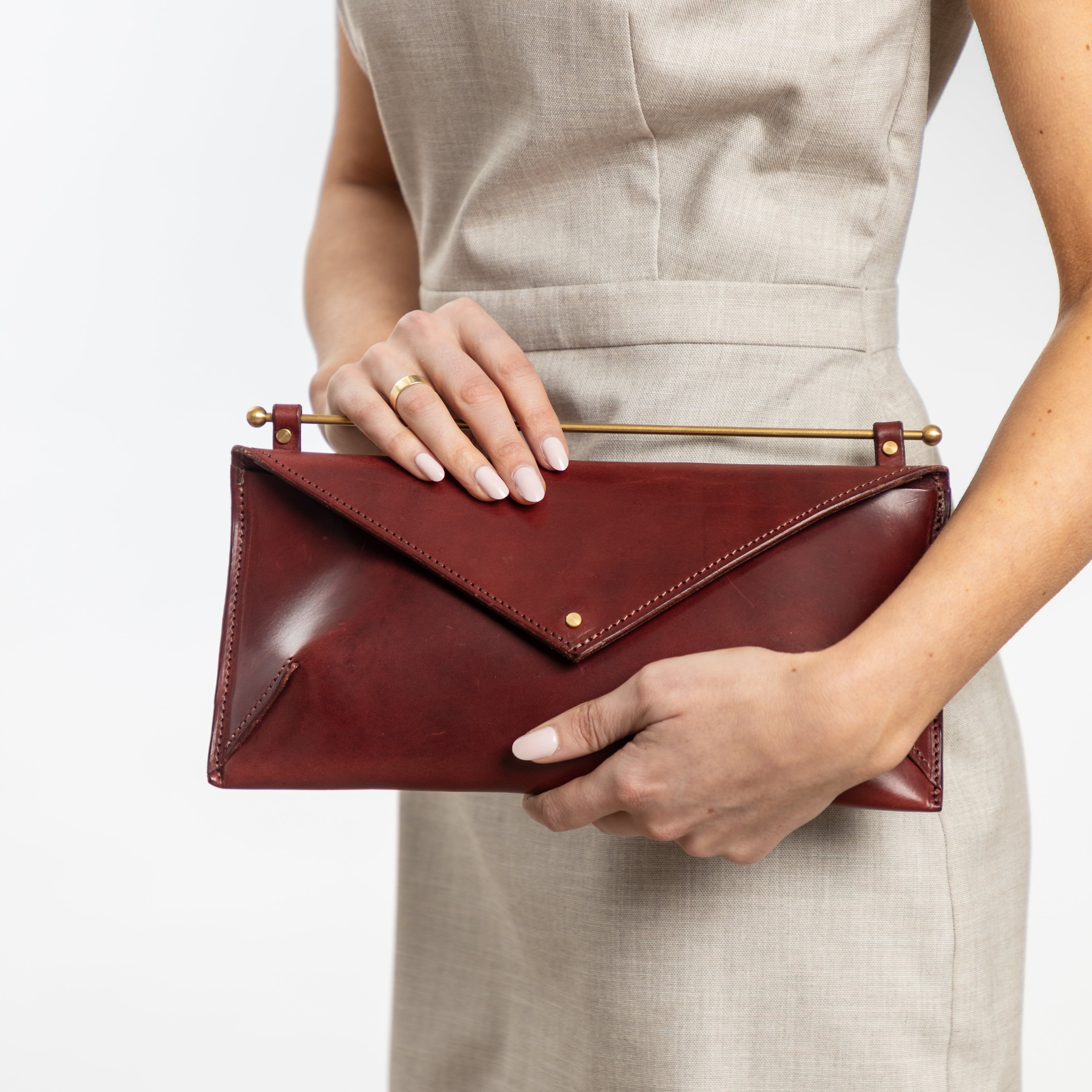 East West Envelope | Oxblood clutch in rich full-grain leather with brass bar detail held by woman in neutral dress