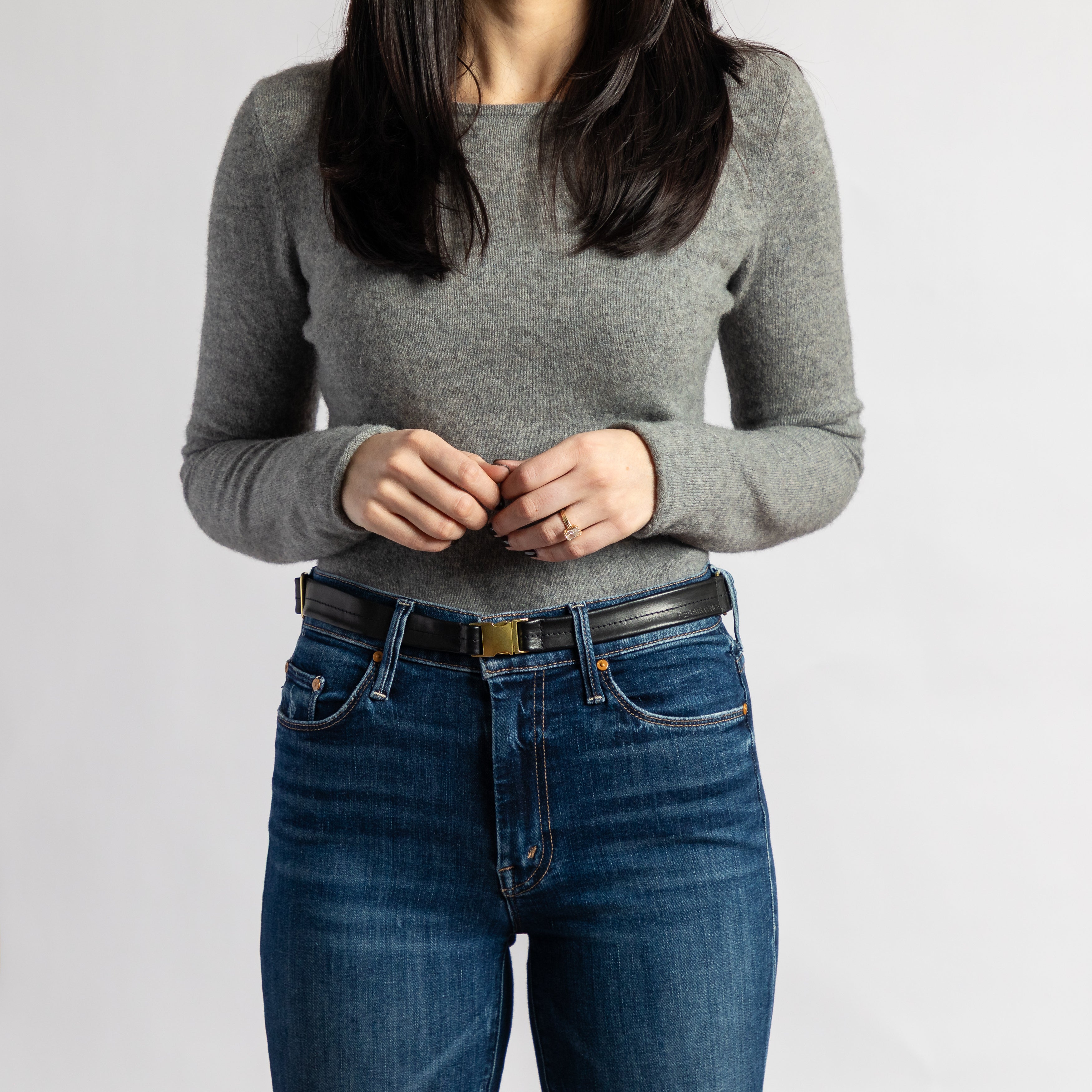 Woman wearing a smooth full-grain leather Festival Bag | Black belt bag with gold-tone hardware over dark denim jeans and gray sweater