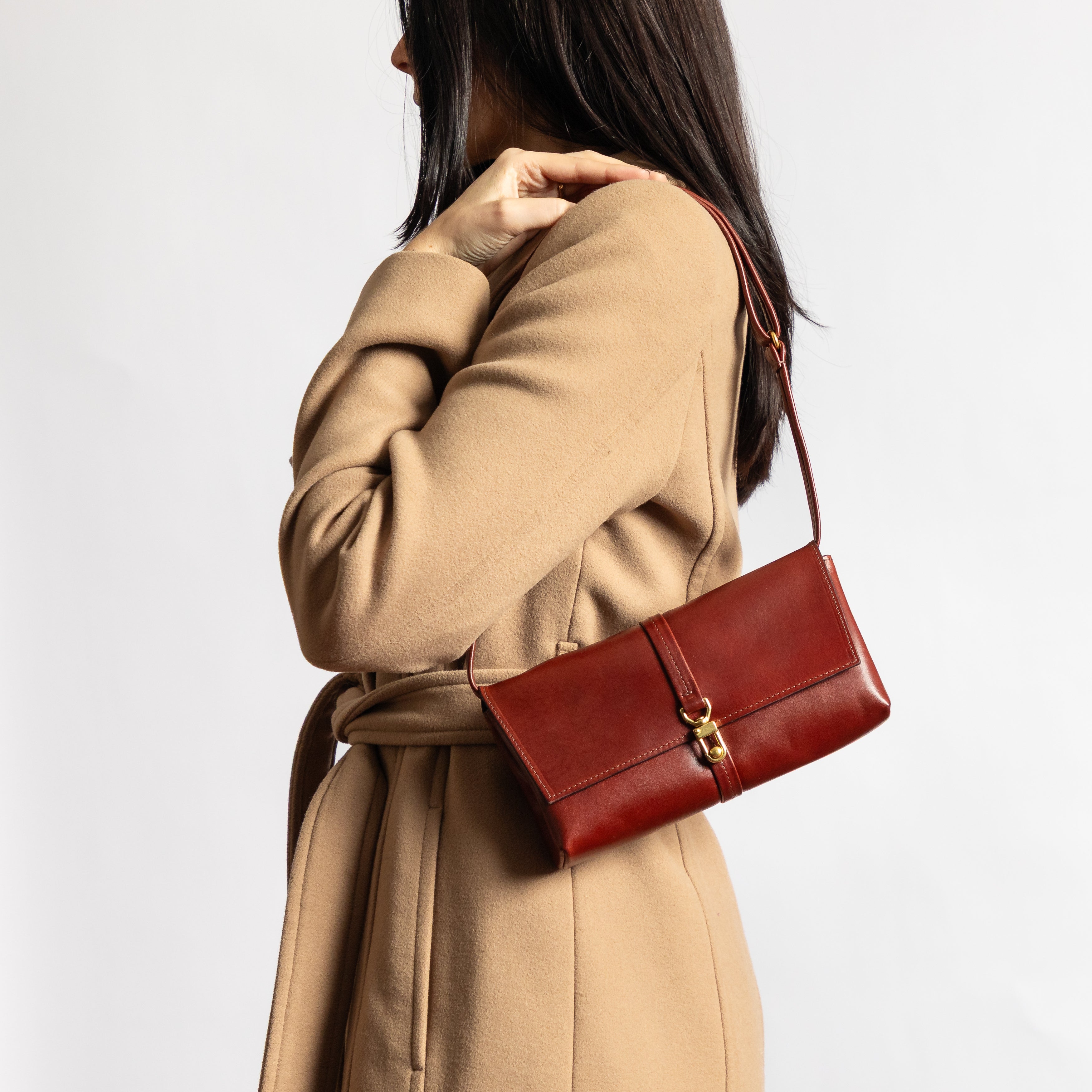 Woman wearing a camel coat carrying a luxury full-grain leather Festival Bag | Sangria with gold hardware clasp and smooth finish