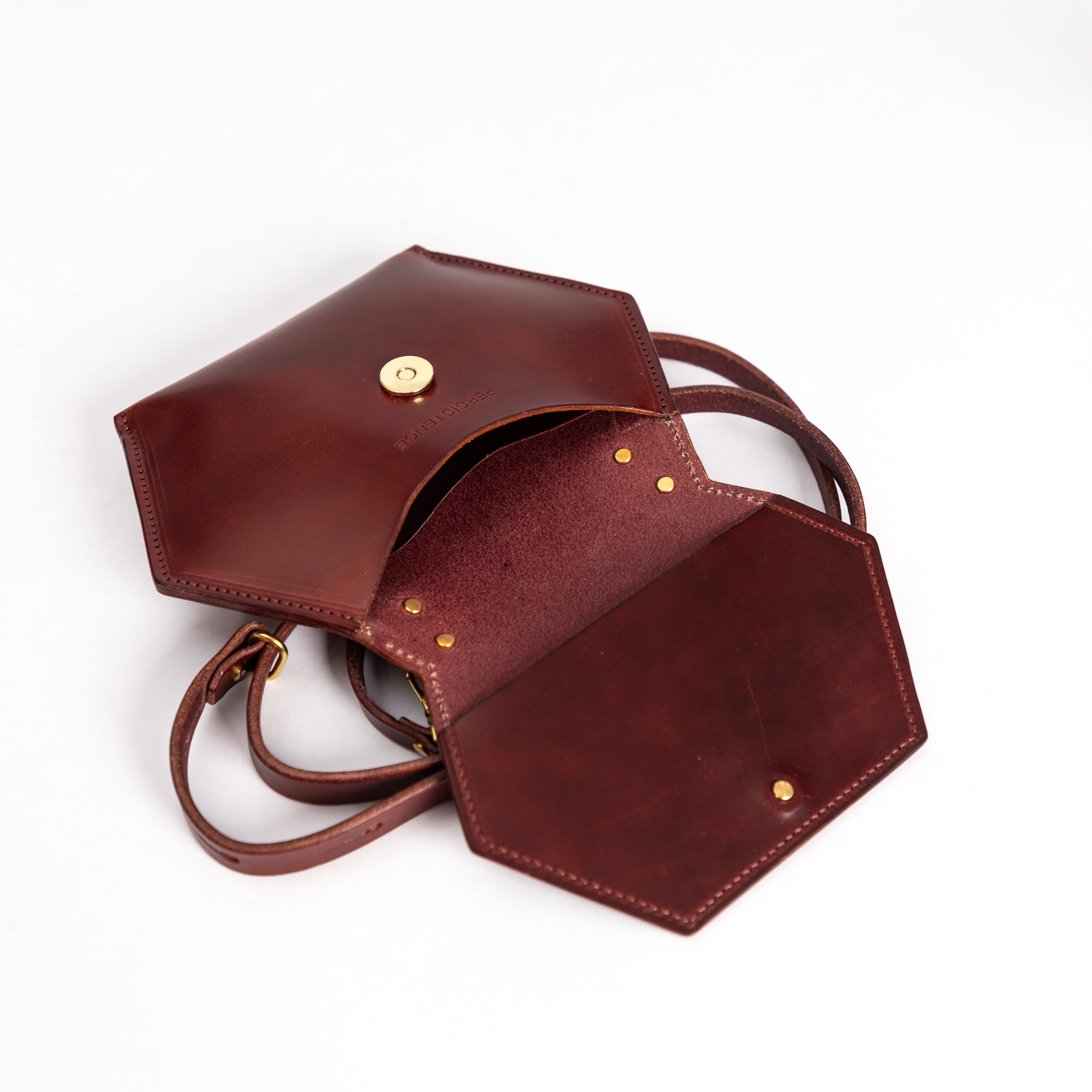 Open oxblood full grain leather honeycomb crossbody bag with gold clasp and removable strap on white background