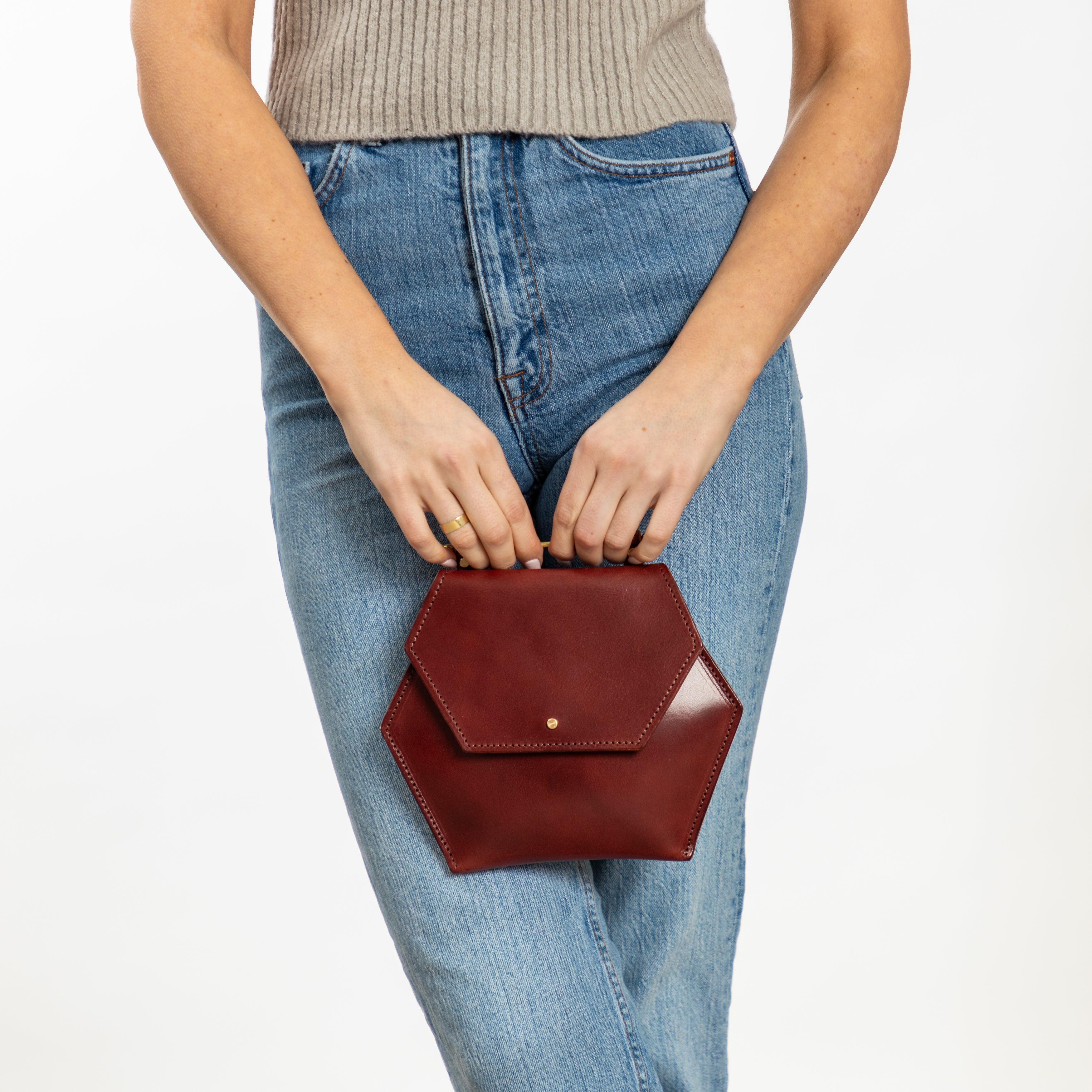 Woman holding oxblood red hexagon-shaped leather crossbody clutch bag with removable strap and pockets