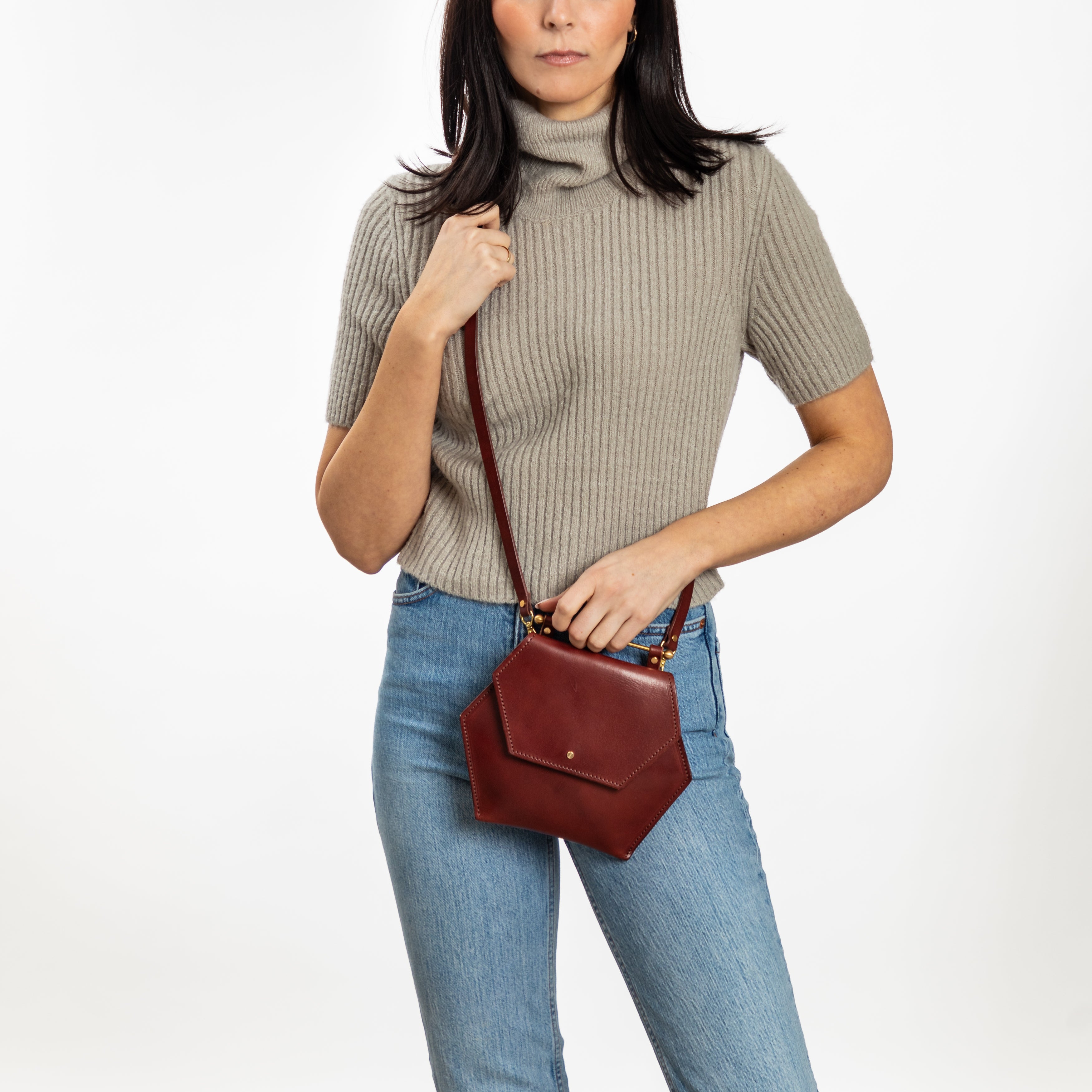 Woman wearing an oxblood hexagon leather crossbody bag with a removable strap and minimalist design