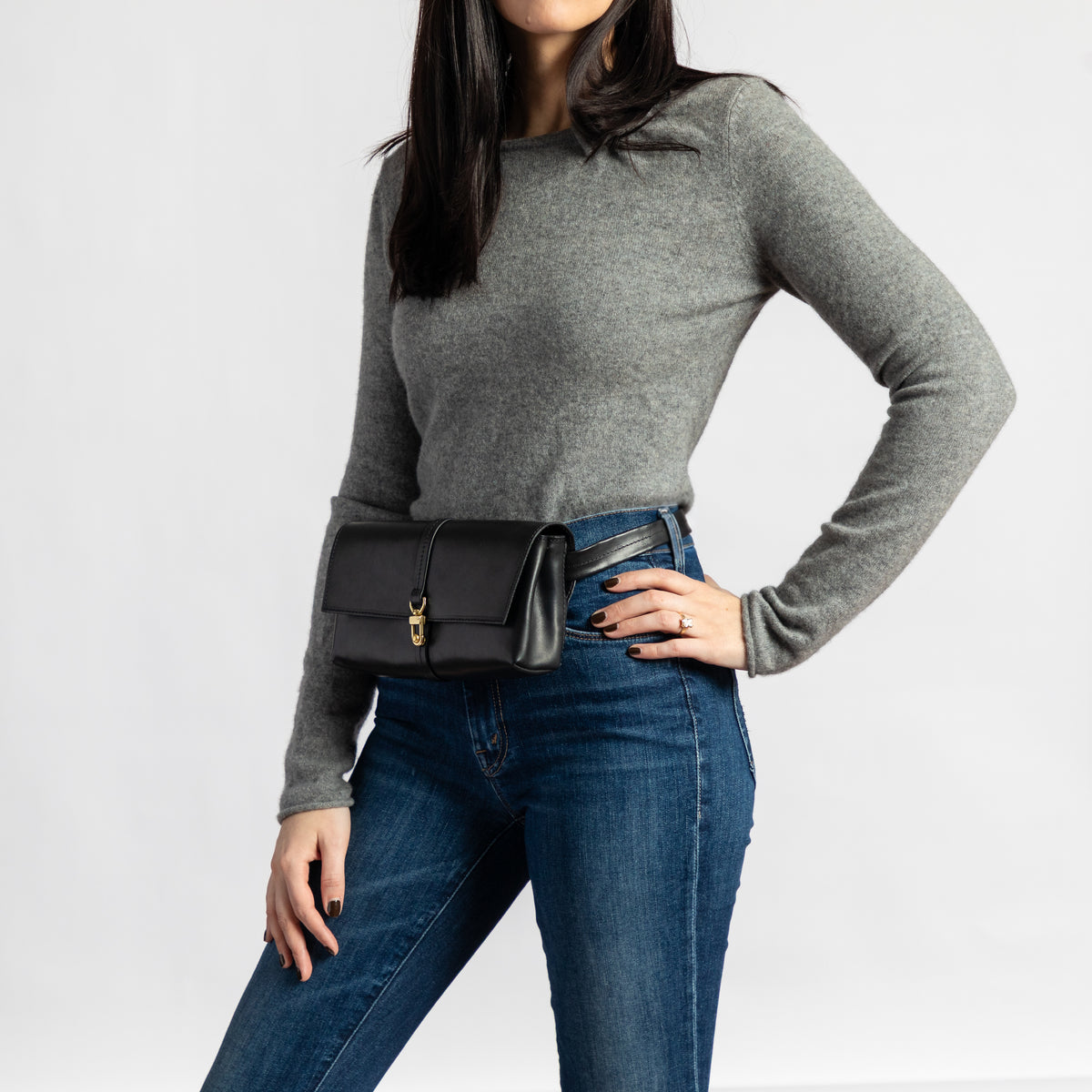 Woman styles a black full-grain vegetable-tanned leather Transpose Bag at the waist with a polished solid brass clasp