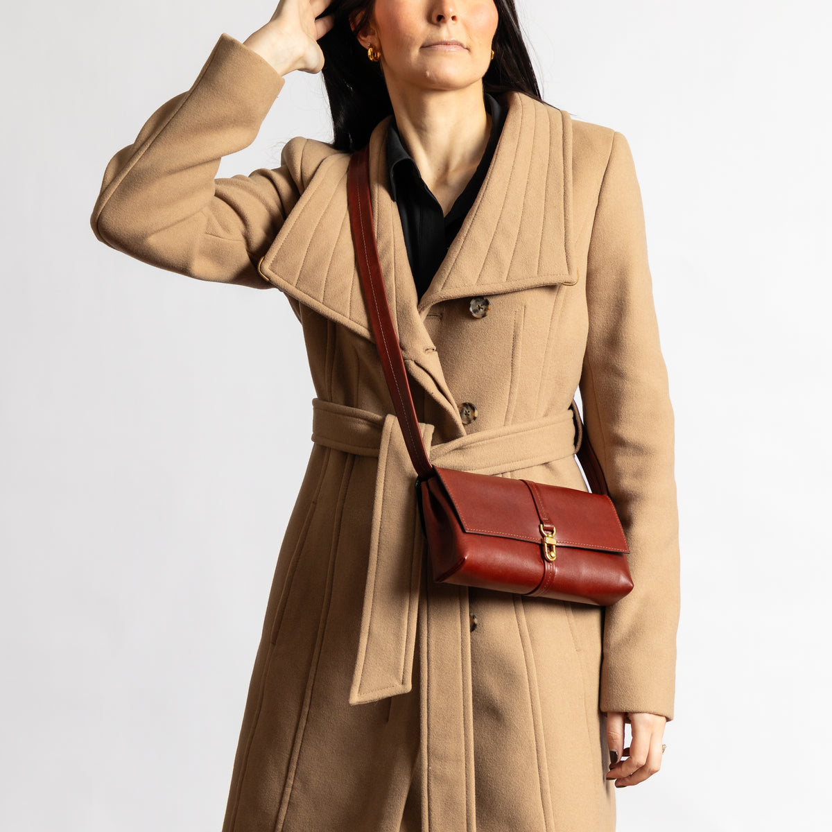 Woman in a camel coat models the Sangria burgundy Transpose Bag crossbody in full-grain vegetable-tanned leather with brass clasp