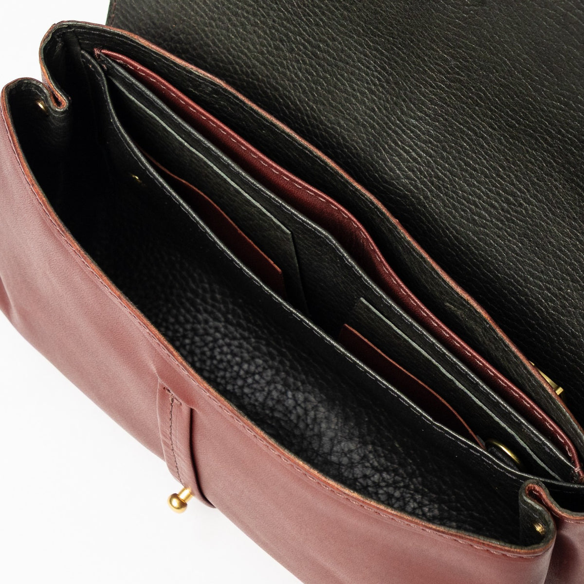 Open sangria burgundy vegetable-tanned leather Transpose Bag revealing a black interior with divided pockets and solid brass hardware