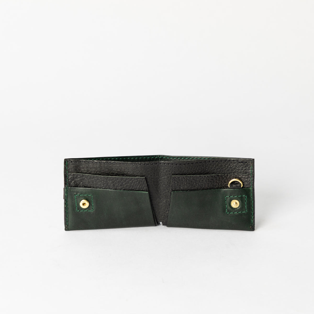 Open dark green and black full-grain leather bifold wallet with card slots and brass snap closures on a white background