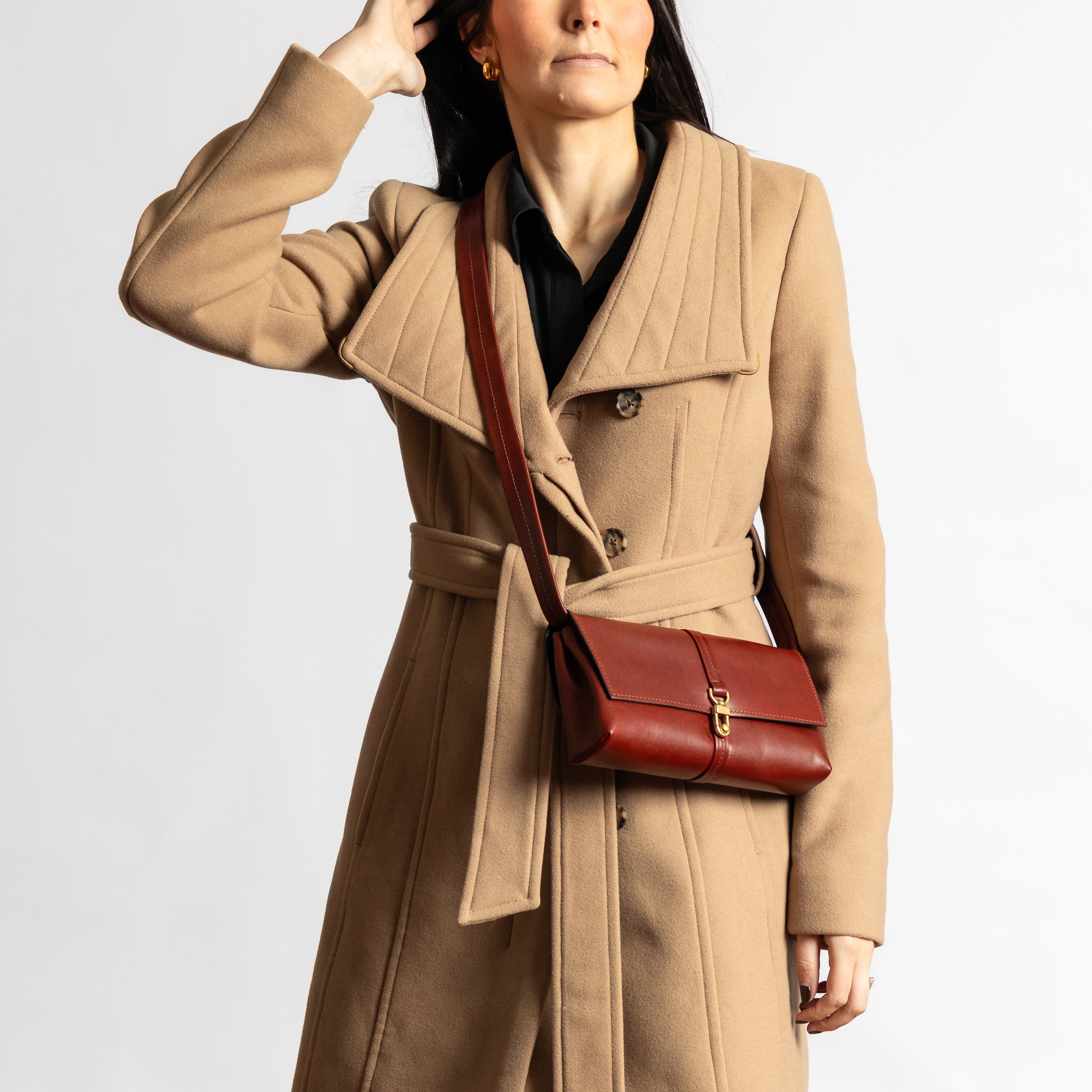 Woman wearing a camel coat carrying a luxury full-grain leather Festival Bag | Sangria crossbody with gold hardware clasp