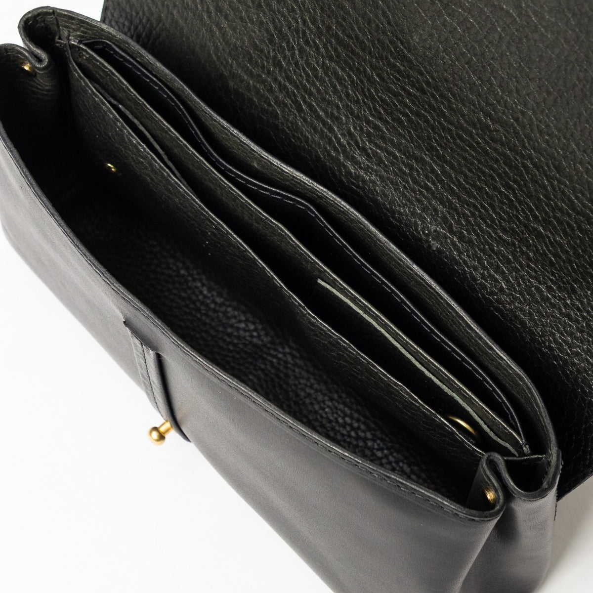 Open black Transpose Bag in full-grain vegetable-tanned leather showing accordion compartments and solid brass hardware