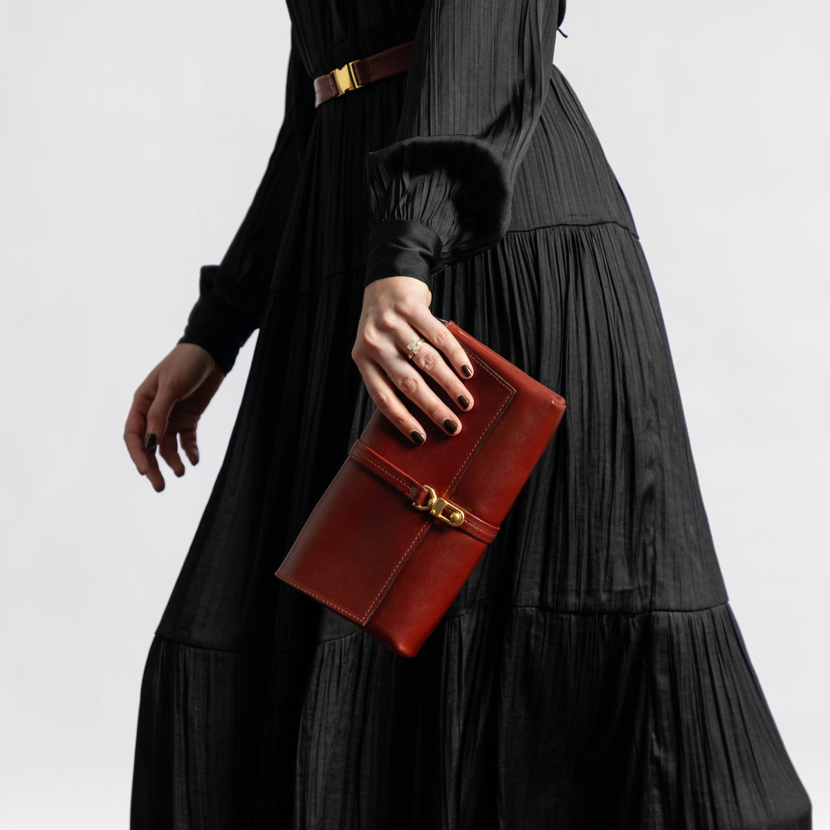 Model in a flowing black dress holds a Sangria burgundy vegetable-tanned leather Transpose Bag as a clutch with a polished brass clasp