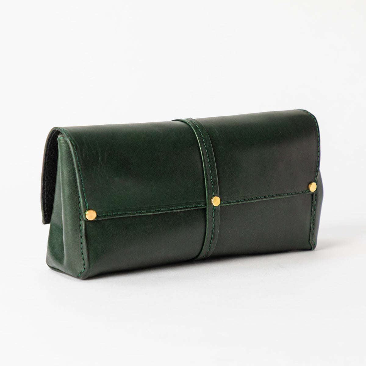 Structured Deep Forest full-grain leather bag with a wraparound center tab side gusset and solid brass studs on white