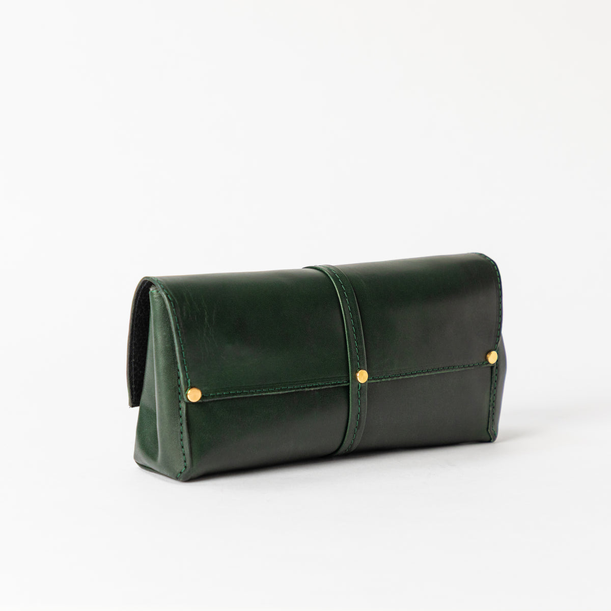 Structured Deep Forest full-grain leather bag with a wraparound center tab side gusset and solid brass studs on white