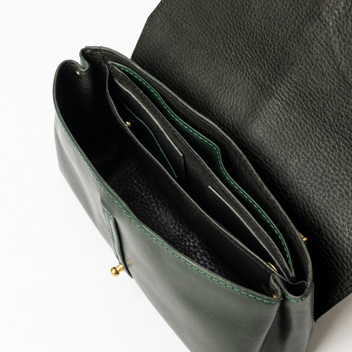 Overhead view of an open dark green leather bag with a black textured flap divided compartments and a small brass clasp