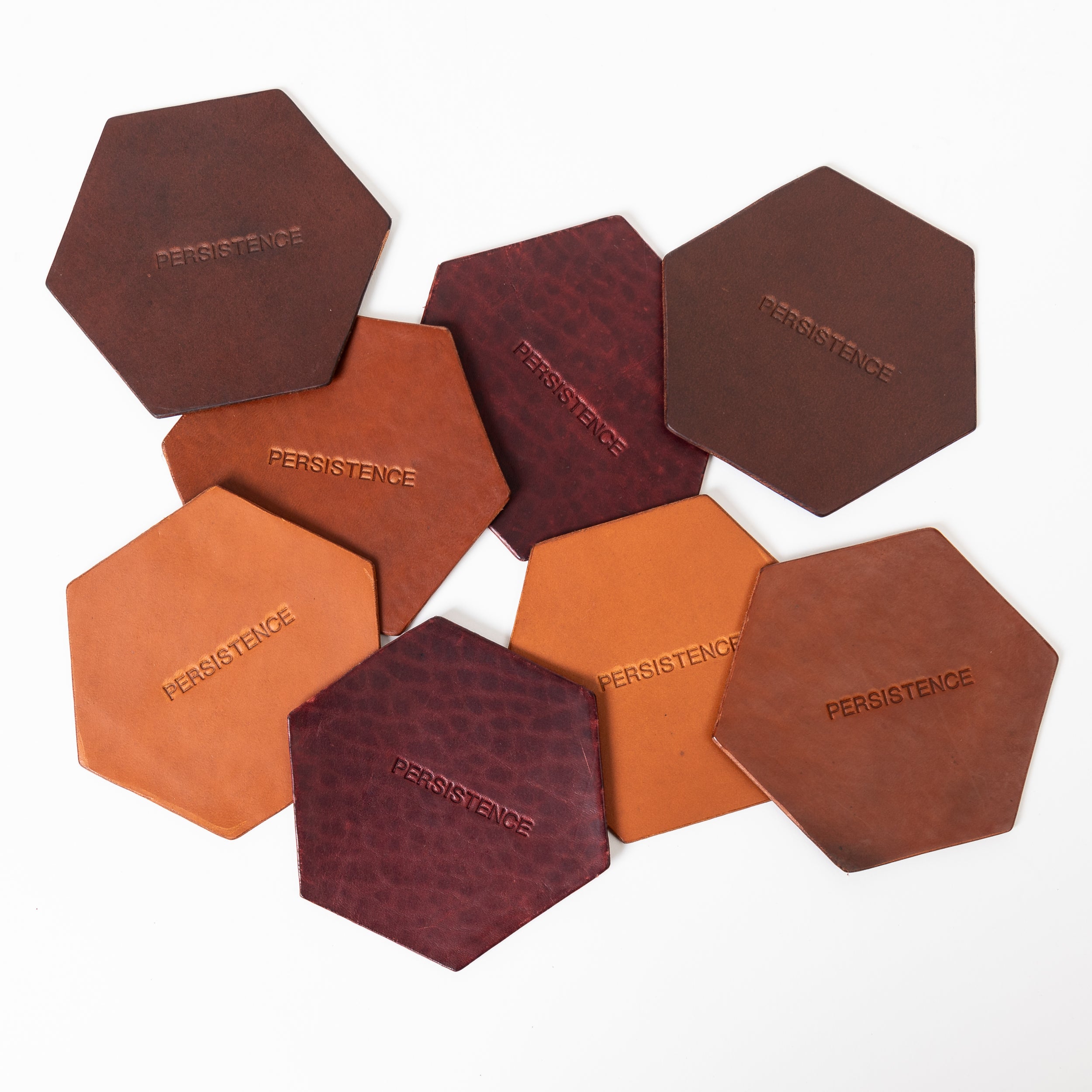 Brown and burgundy leather coasters stamped with PERSISTENCE scattered on a white background.